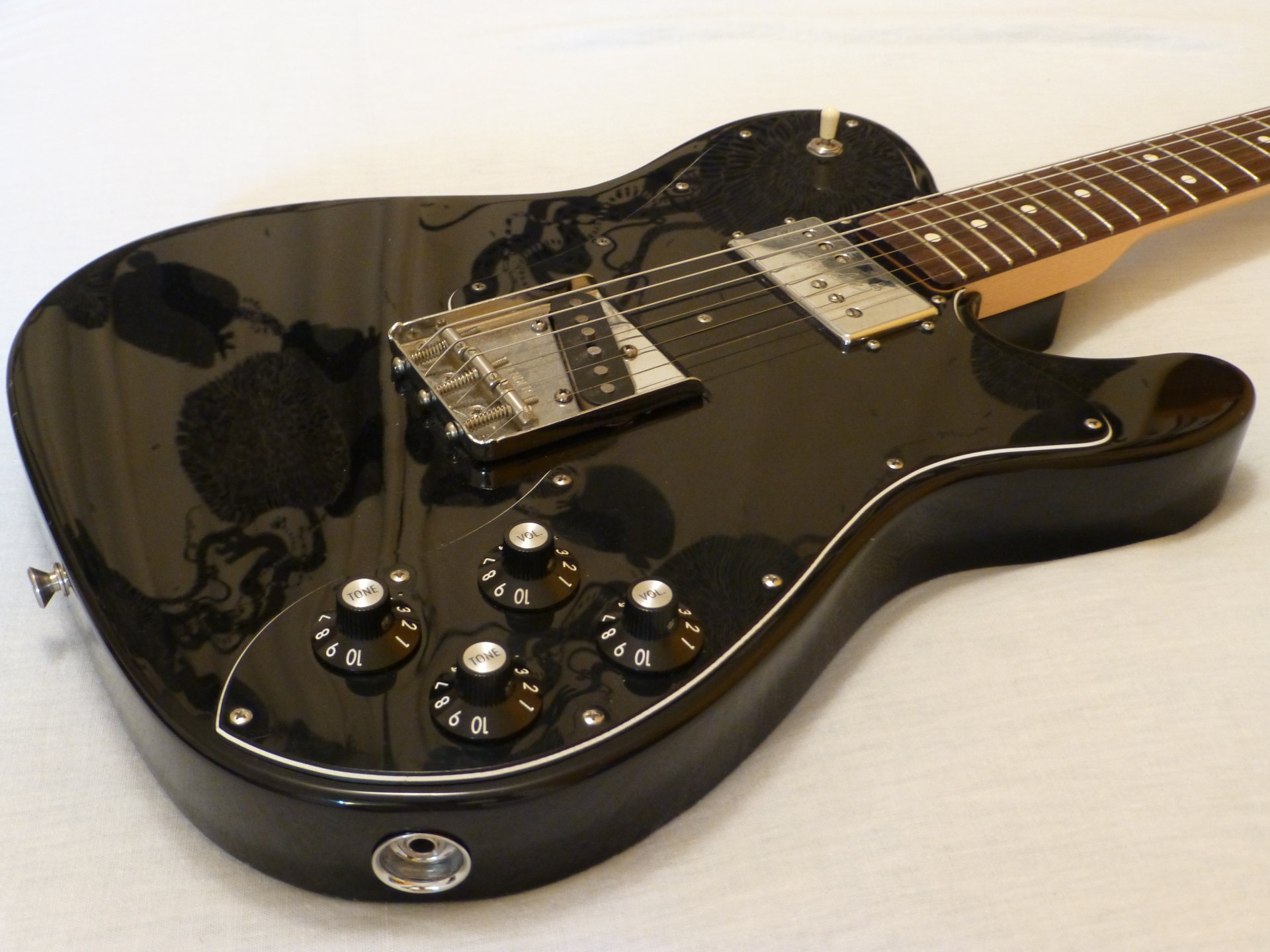 Close-up of a glossy black electric guitar on a light surface, detailed strings and knobs — 4K Ultra HD PC desktop wallpaper background, music-themed.