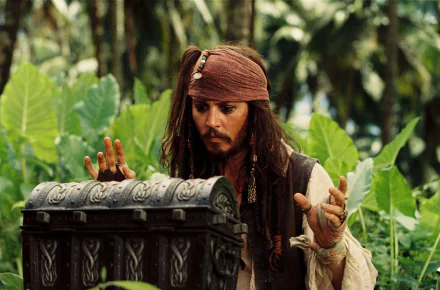 Jack Sparrow, played by Johnny Depp, appears intrigued as he examines a chest surrounded by lush greenery in a scene from *Pirates of the Caribbean: Dead Man's Chest*.
