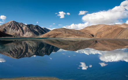 HD PC desktop wallpaper: Pangong Lake nature scene — glassy blue water mirroring barren mountains and drifting clouds beneath a vivid sky.