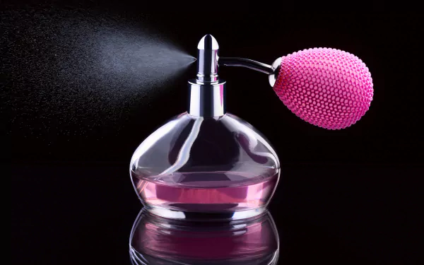 A stunning HD desktop wallpaper featuring a vintage perfume bottle with a pink atomizer, capturing the elegance of fragrance photography against a sleek black background.
