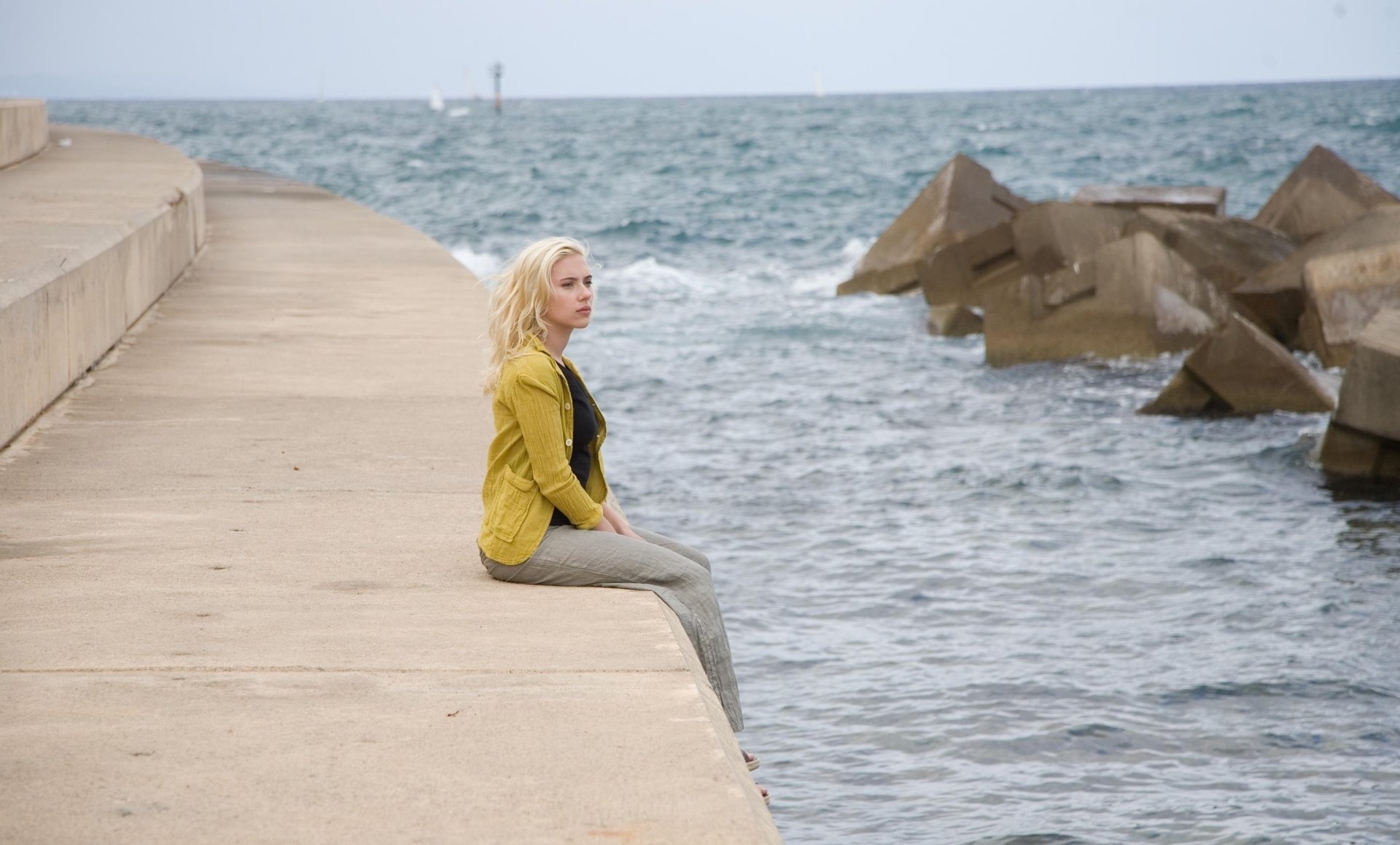 Scarlett Johansson in a scene from the movie Vicky Cristina Barcelona, sitting on a concrete dock by the ocean, HD PC desktop wallpaper and background.