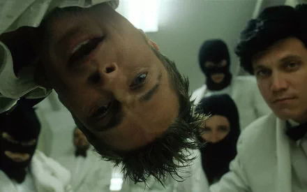 A scene from the movie Fight Club featuring Brad Pitt in a close-up shot, surrounded by individuals in masks, creating an intense and dramatic atmosphere. HD desktop wallpaper.