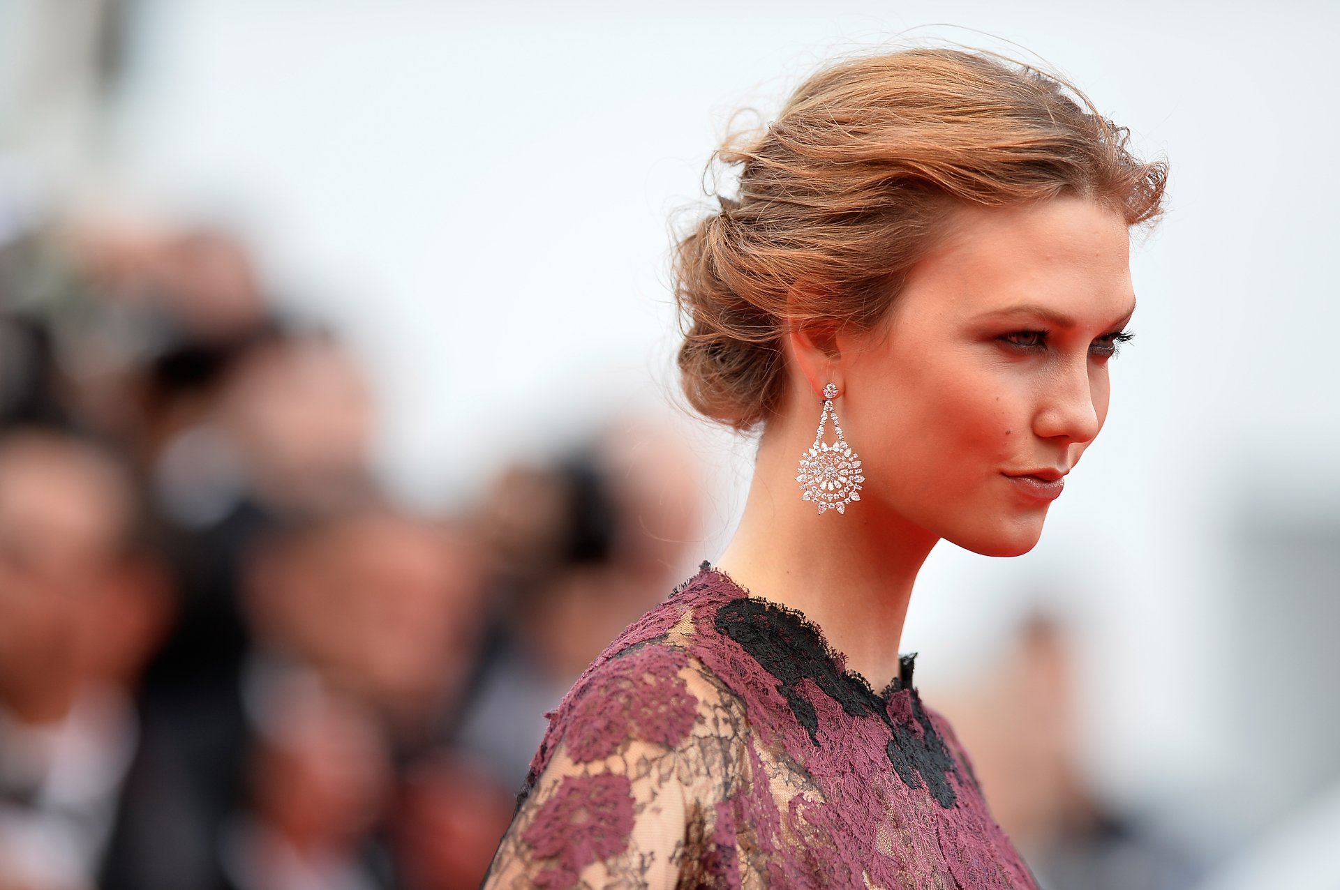 HD PC desktop wallpaper featuring celebrity Karlie Kloss in an elegant lace dress and statement earrings, captured in a side profile at a formal event.