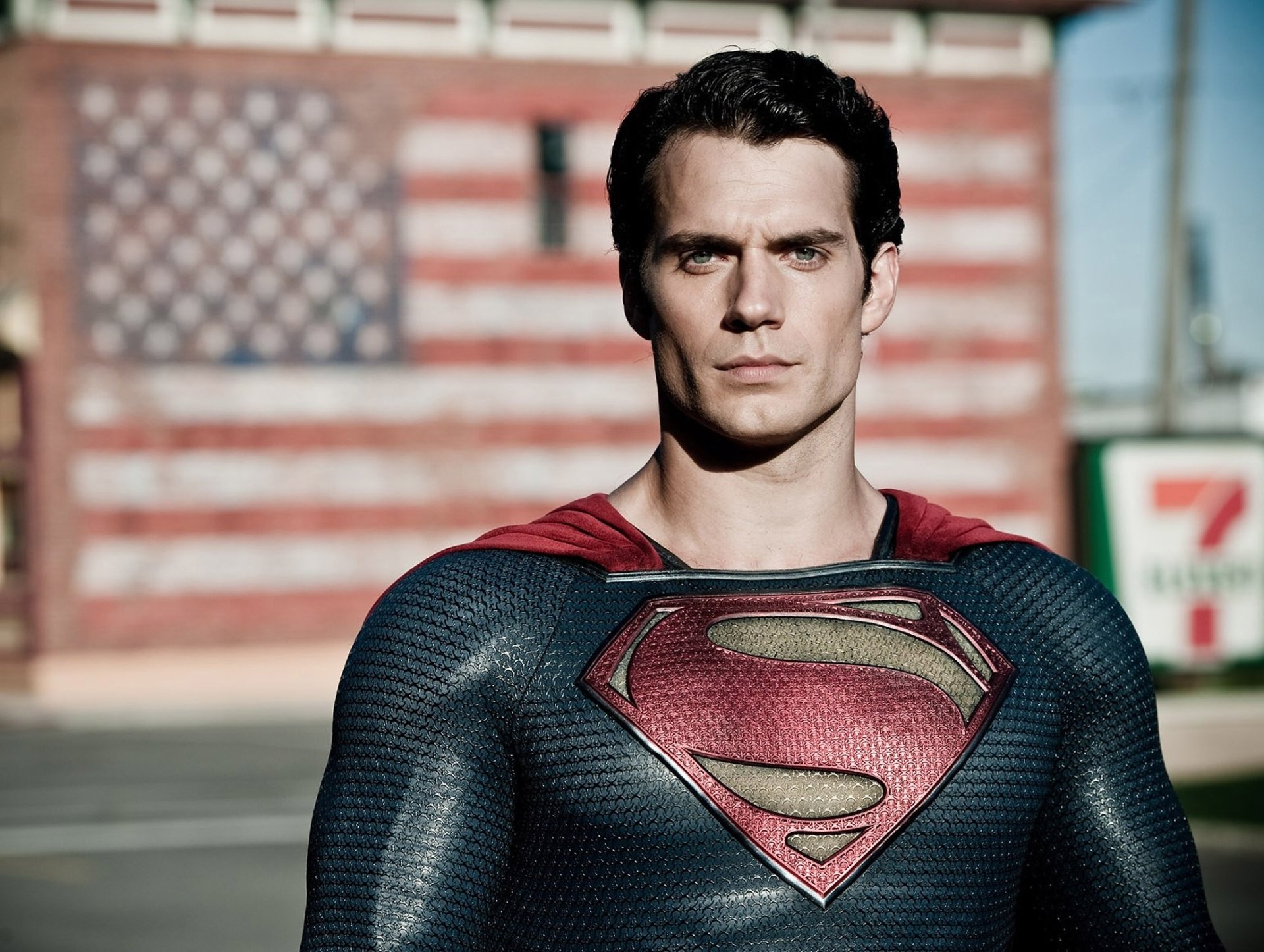 Henry Cavill as Superman in Man of Steel, striking a powerful pose with an American flag backdrop, featured as an HD wallpaper for fans of the iconic movie.