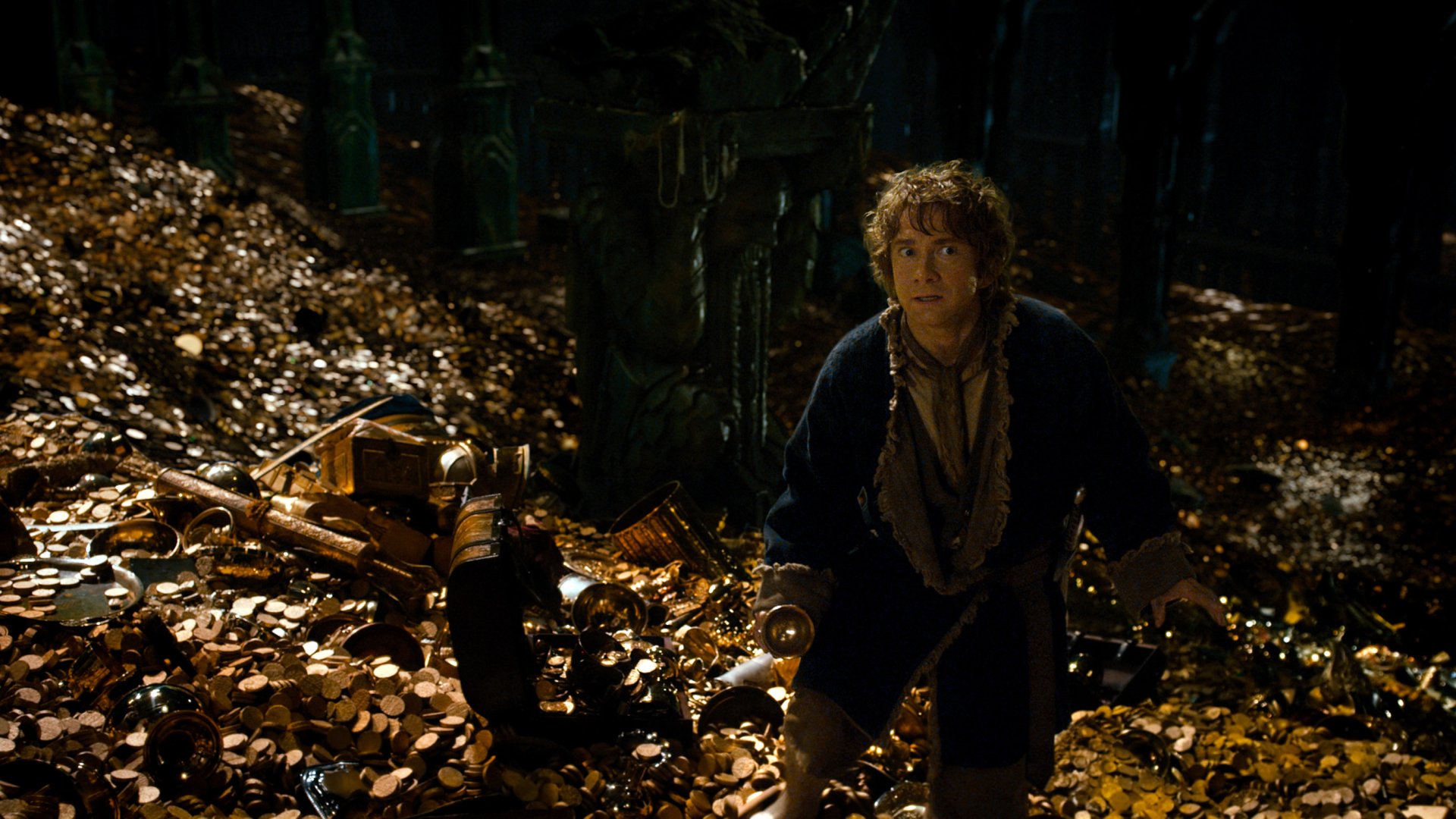 2K Quad HD PC desktop wallpaper from The Hobbit: The Desolation of Smaug — Bilbo stands amid heaps of gold and treasure in a dim, shadowed cavern.