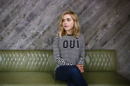 HD PC desktop wallpaper featuring celebrity Kiernan Shipka seated on a green leather couch against a textured gray wall, wearing a black and white striped shirt.