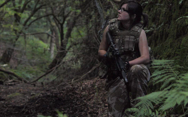 HD PC desktop wallpaper featuring a woman from Girls & Guns, dressed in tactical gear and holding a rifle while crouching in a dense forest.