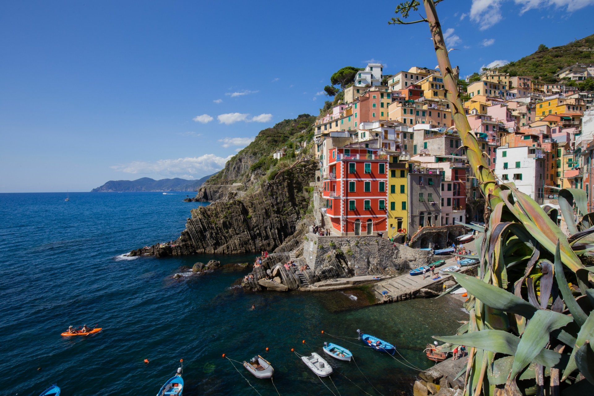 Colorful man-made village of Riomaggiore in Italy's Cinque Terre, perched on cliffs overlooking the blue sea under a clear sky, captured in 4K Ultra HD quality.