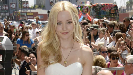 A confident Dove Cameron smiles in a white dress, surrounded by fans at an event. This HD image serves as a vibrant desktop wallpaper.