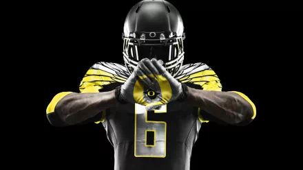 HD PC desktop wallpaper background: Oregon Ducks football player in black-and-yellow uniform making the O hand sign, dramatic sports portrait on a black backdrop.