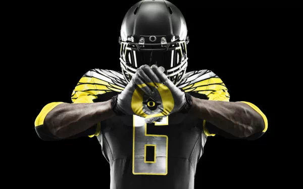 HD PC desktop wallpaper background: Oregon Ducks football player in black-and-yellow uniform making the O hand sign, dramatic sports portrait on a black backdrop.