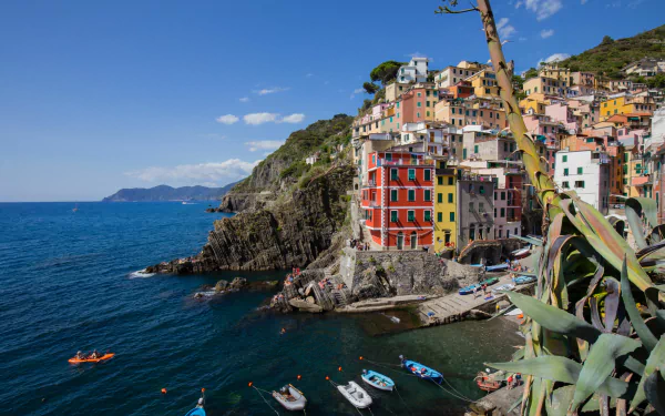 Colorful man-made village of Riomaggiore in Italy's Cinque Terre, perched on cliffs overlooking the blue sea under a clear sky, captured in 4K Ultra HD quality.