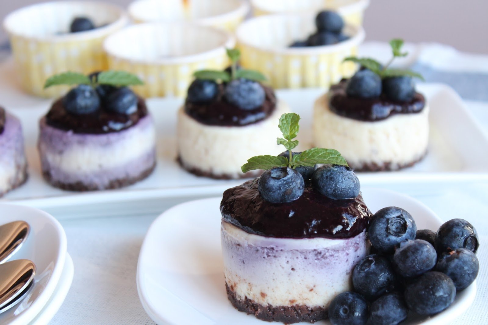 HD PC desktop wallpaper featuring close-up of mini cheesecakes topped with blueberries and mint leaves, surrounded by fresh blueberries on a white plate and tray.