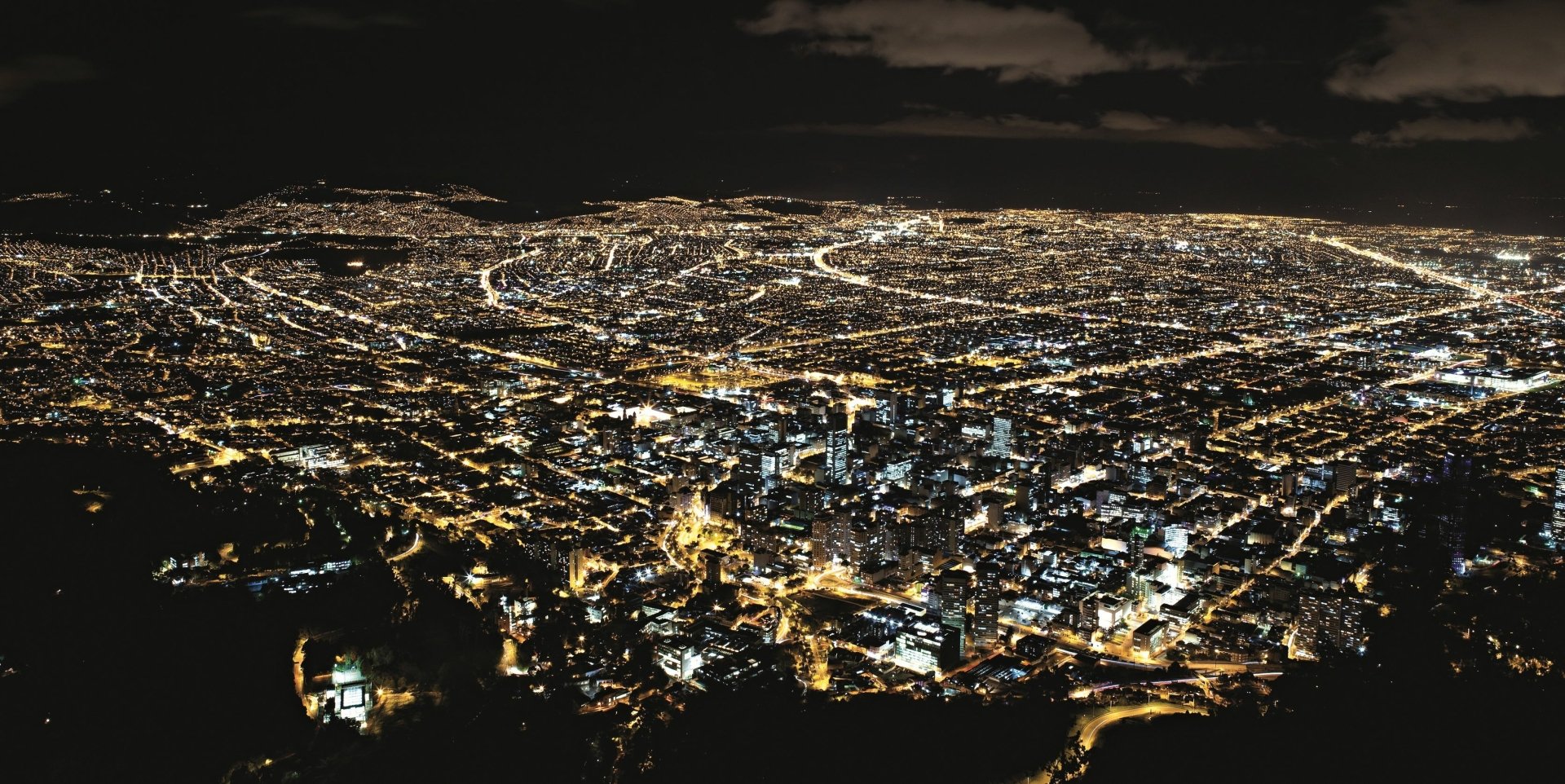 Aerial view of man-made cityscape of Bogotá illuminated at night, captured in high-definition for a PC desktop wallpaper and background.