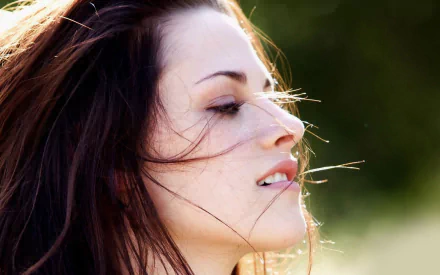 A captivating HD wallpaper featuring celebrity Kristen Stewart, showcasing her profile with wind-swept hair against a natural backdrop.