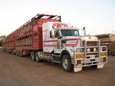 HD desktop wallpaper of a Marmon road train vehicle with multiple red livestock trailers parked on a dirt road under a clear sky.