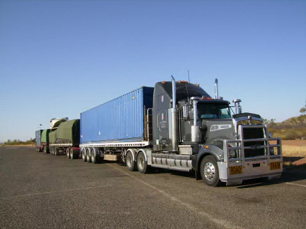 HD PC desktop wallpaper featuring a Kenworth vehicle hauling large cargo on a clear day along a rural road.