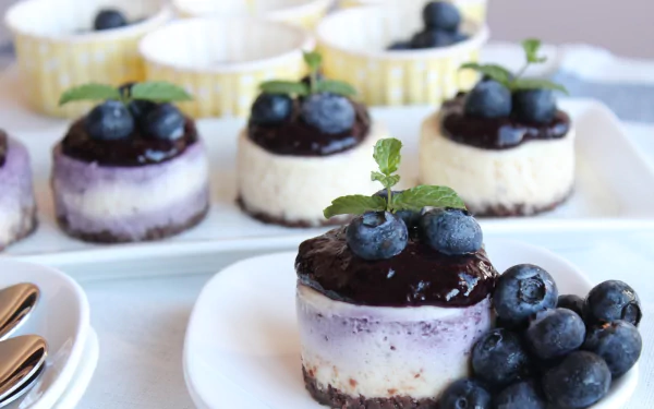 HD PC desktop wallpaper featuring close-up of mini cheesecakes topped with blueberries and mint leaves, surrounded by fresh blueberries on a white plate and tray.