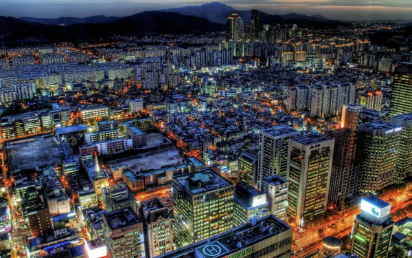 A stunning HD desktop wallpaper of Seoul at night, showcasing a vibrant cityscape filled with illuminated buildings and bustling streets against a backdrop of mountains.