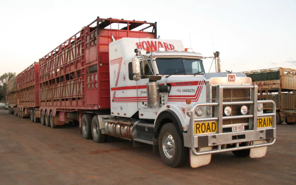 HD desktop wallpaper of a Marmon road train vehicle with multiple red livestock trailers parked on a dirt road under a clear sky.