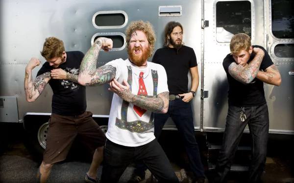 HD PC desktop wallpaper of the metal band Mastodon posing energetically in front of a metallic trailer, showcasing their tattooed arms and intense expressions.