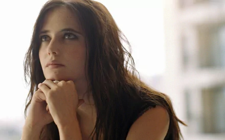A serene HD desktop wallpaper featuring Eva Green, gazing thoughtfully with her chin resting on her hands, illuminated by soft natural light.