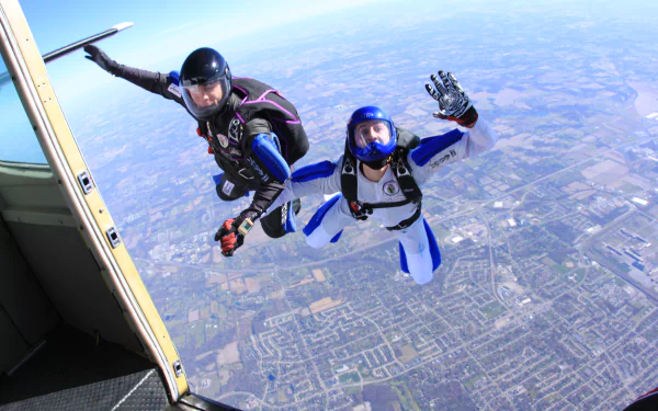 Two skydivers in midair above a cityscape, captured in vibrant 4K Ultra HD, showcasing the thrill of the sport against a clear blue sky.