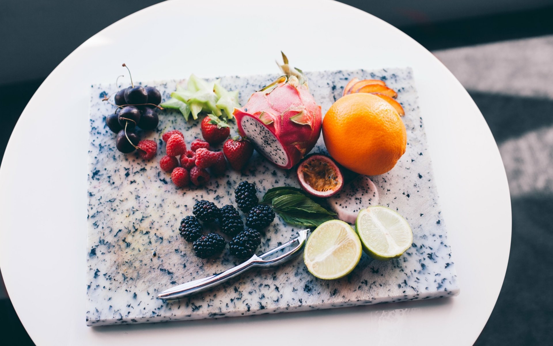 HD desktop wallpaper featuring a still life arrangement of vibrant fruits including pitaya, raspberry, orange, lime, cherry, blackberry, star fruit, and strawberry on a marble board.