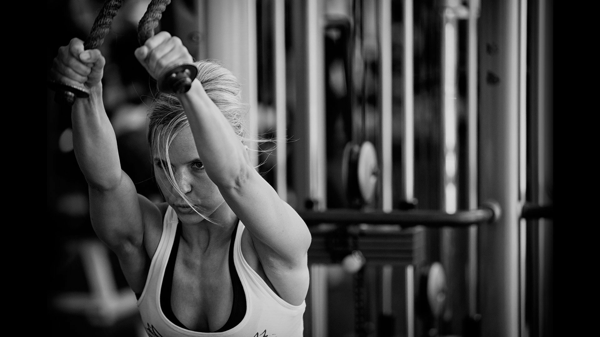 Black and white HD desktop wallpaper of a focused woman performing battle rope exercises in a gym, highlighting strength and dedication in fitness and sports.