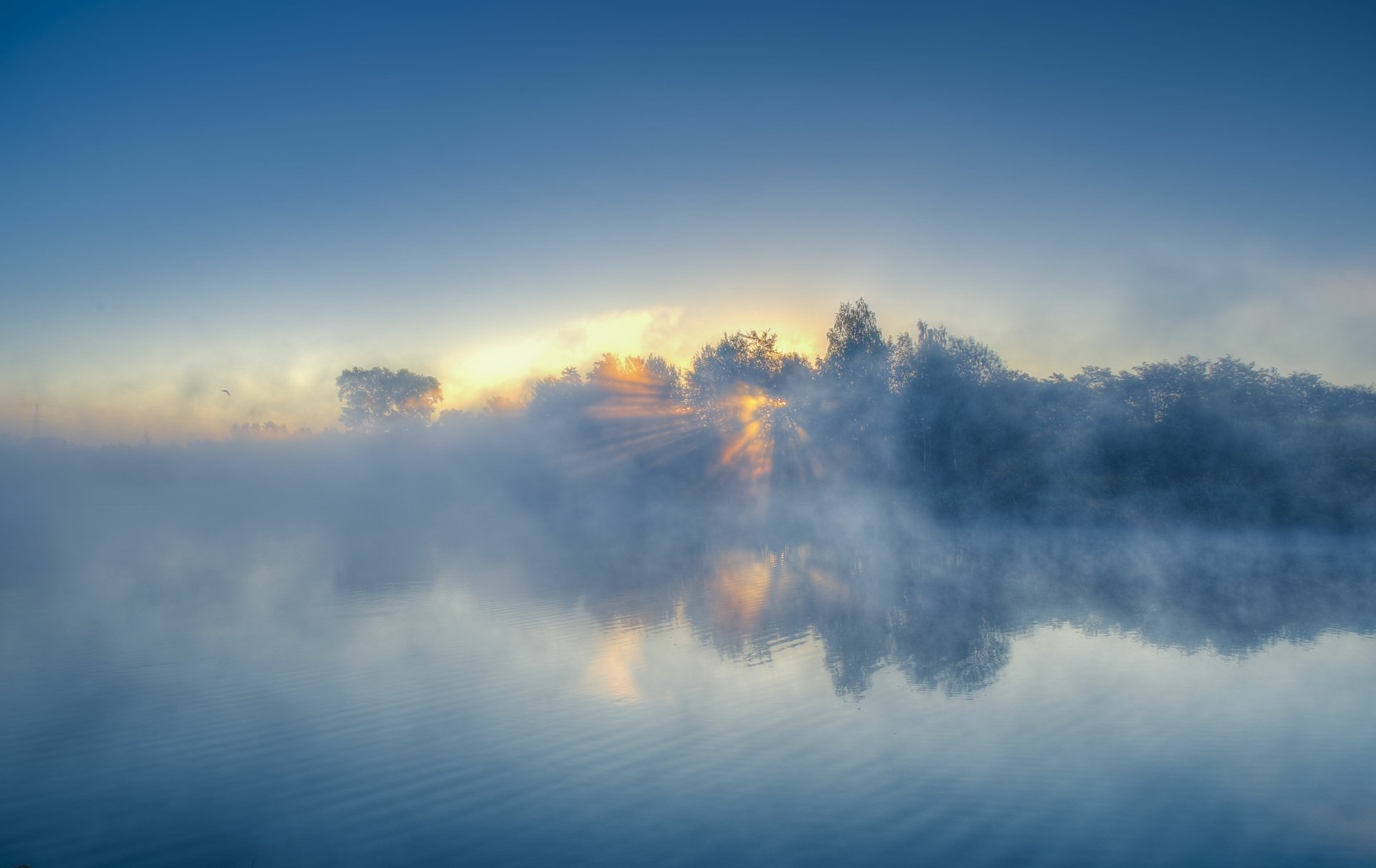 A serene sunrise over a fog-covered river, highlighting the beauty of nature with soft reflections on the water. This stunning 4K Ultra HD image serves as a captivating desktop wallpaper.