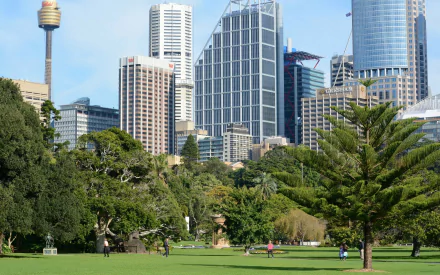 A vibrant scene of the Royal Botanic Gardens in Sydney, Australia, with people enjoying the park, lush trees, and towering city buildings in the background.