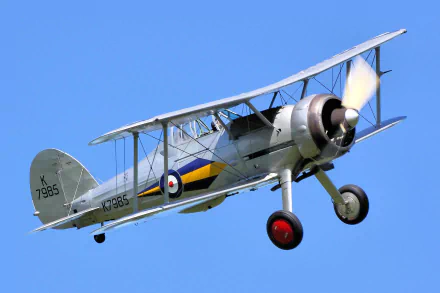HD PC desktop wallpaper: military Gloster Gladiator biplane in flight against a clear blue sky, RAF roundel and serial markings visible.