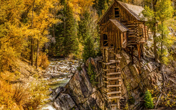 HDR 4K Ultra HD desktop wallpaper of man-made Crystal Mill perched on a rocky ledge above a rushing stream, surrounded by golden autumn trees.