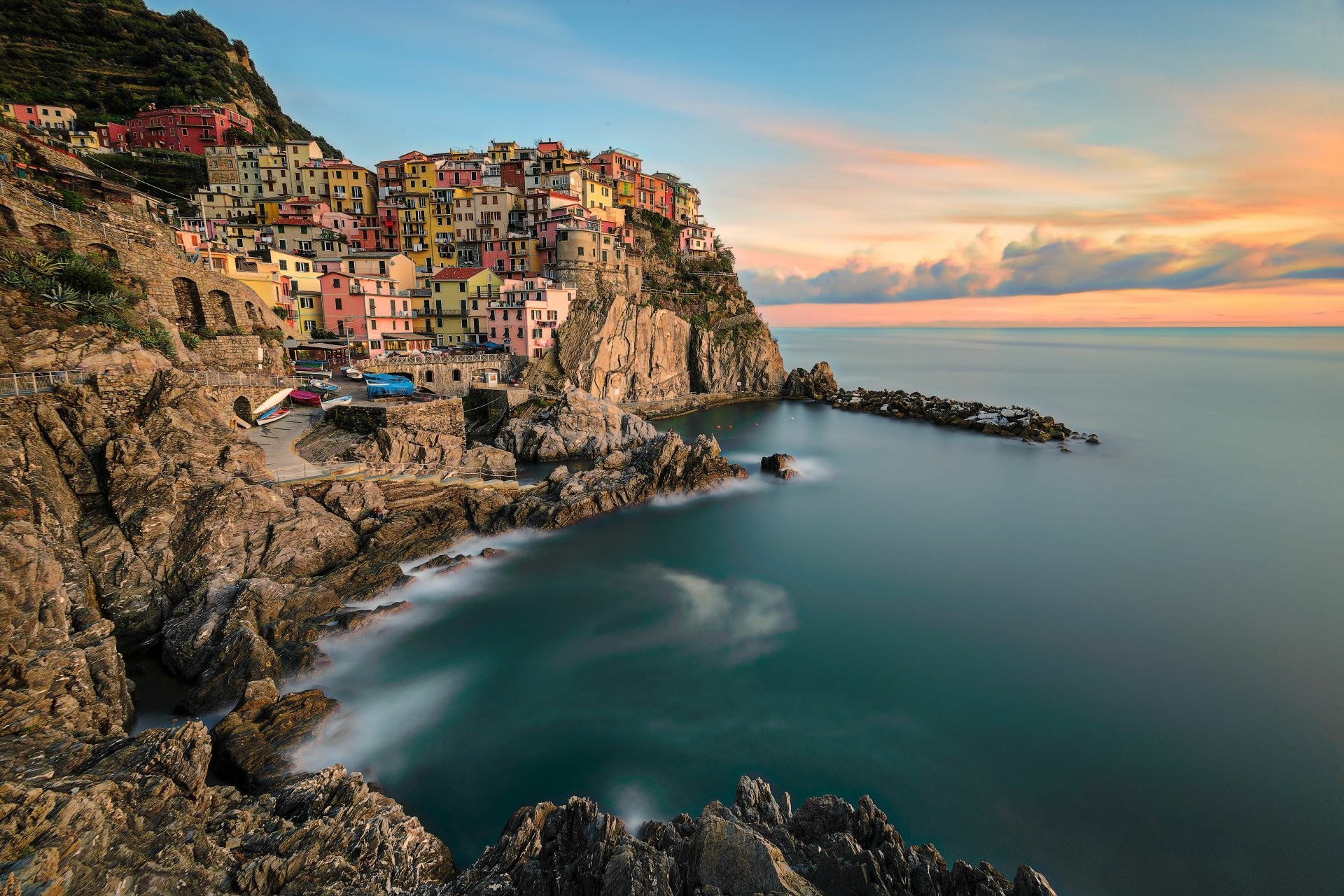 4K Ultra HD man-made coastal village of Manarola perched on rocky cliffs overlooking a calm sea during sunset, captured in vibrant colors for a PC desktop wallpaper.