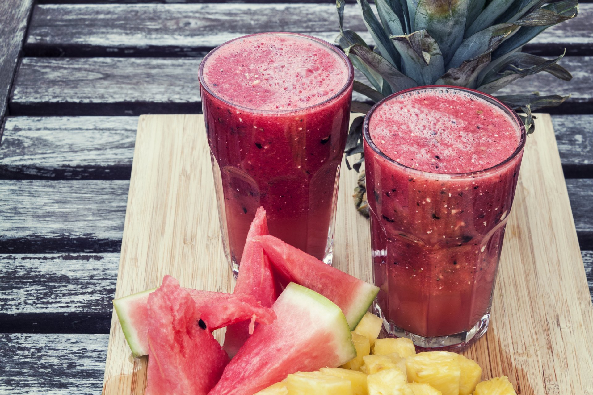 Two glasses of vibrant watermelon and pineapple juice sit on a wooden board, accompanied by fresh fruit pieces, creating a refreshing and colorful smoothie scene in 4K Ultra HD.