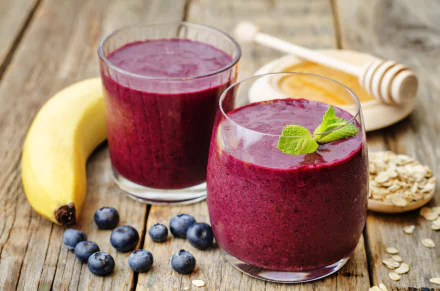 Two glasses of vibrant blueberry and banana smoothie sit on a wooden table, accompanied by fresh blueberries, honey, and oats, creating a refreshing and colorful food scene in 4K Ultra HD.