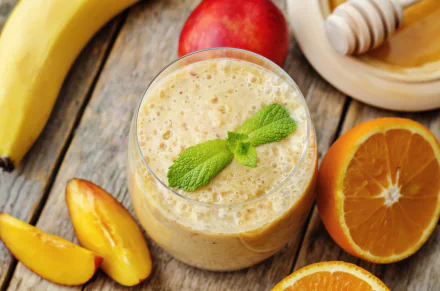 A vibrant 4K Ultra HD wallpaper featuring a creamy smoothie garnished with mint, surrounded by fresh orange slices, banana, peach, and honey on a rustic wooden surface.
