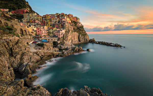 4K Ultra HD man-made coastal village of Manarola perched on rocky cliffs overlooking a calm sea during sunset, captured in vibrant colors for a PC desktop wallpaper.