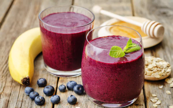 Two glasses of vibrant blueberry and banana smoothie sit on a wooden table, accompanied by fresh blueberries, honey, and oats, creating a refreshing and colorful food scene in 4K Ultra HD.