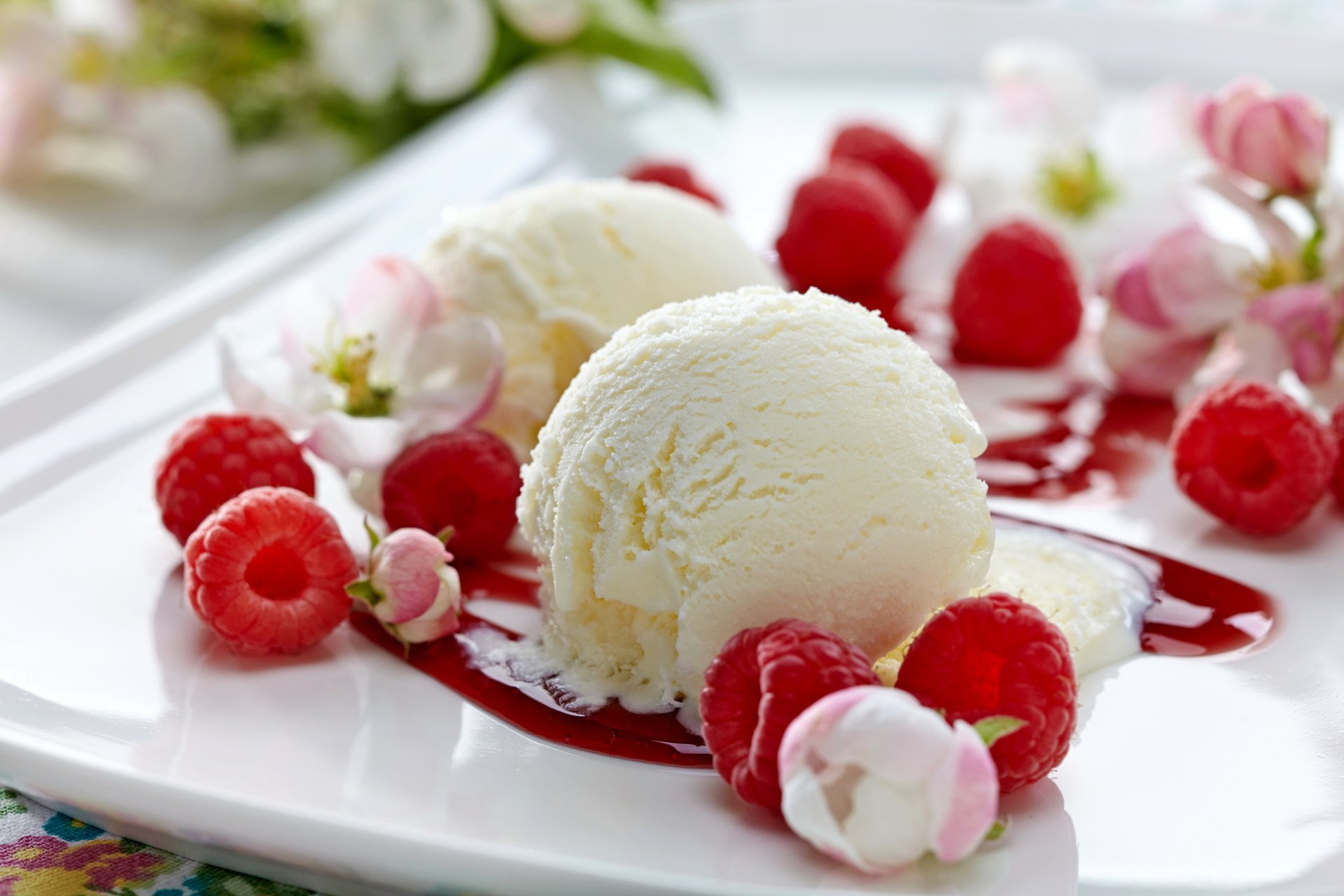 A delicious dessert featuring scoops of ice cream surrounded by fresh raspberries and drizzled with raspberry sauce, beautifully arranged on a white plate. A vibrant 4K Ultra HD wallpaper.