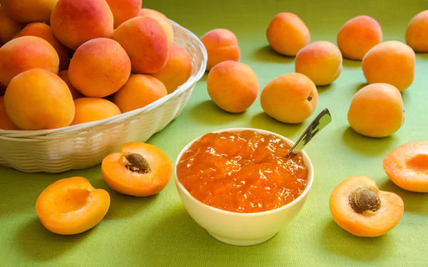 4K Ultra HD desktop wallpaper featuring fresh apricots scattered on a green surface with a bowl of apricot jam and a white basket filled with apricots.