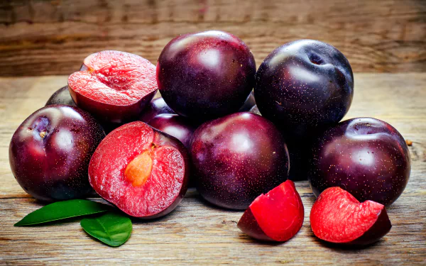 Close-up of fresh, ripe plums with a wooden background, captured in vibrant 4K Ultra HD quality for a vivid PC desktop wallpaper featuring natural fruit imagery.