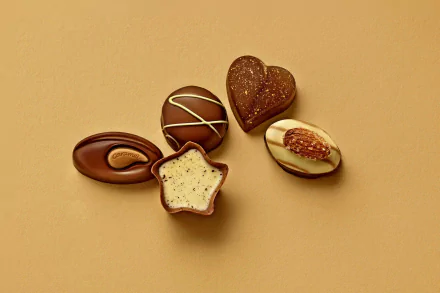 HD desktop wallpaper featuring an assortment of almond-topped and heart-shaped chocolates and candies on a warm beige background.