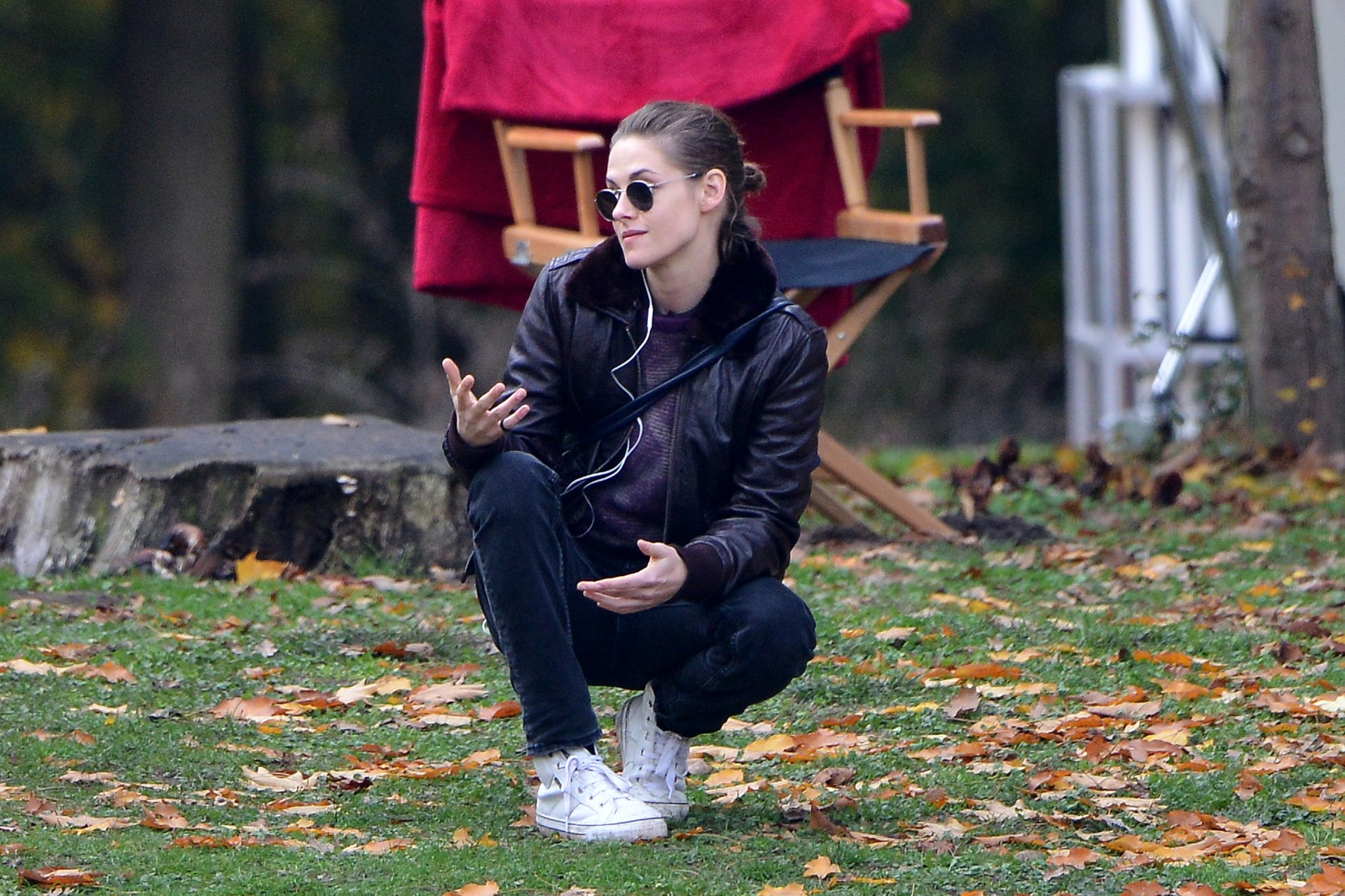 Kristen Stewart is captured in a candid moment outdoors, dressed in a leather jacket and sunglasses, surrounded by autumn leaves, making for a striking 4K Ultra HD wallpaper.