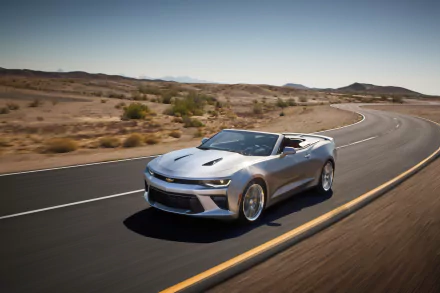 A sleek silver Chevrolet Camaro SS convertible drives along a winding road in a desert landscape, showcasing its powerful design against the vast, arid scenery.