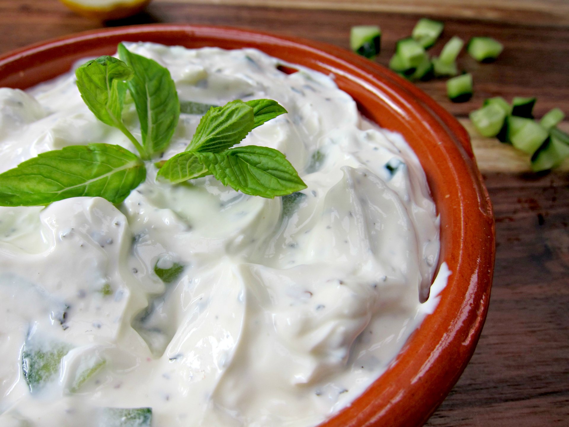 Close-up of creamy tzatziki topped with mint in a terracotta bowl on wood; 2K Quad HD PC desktop wallpaper/background.