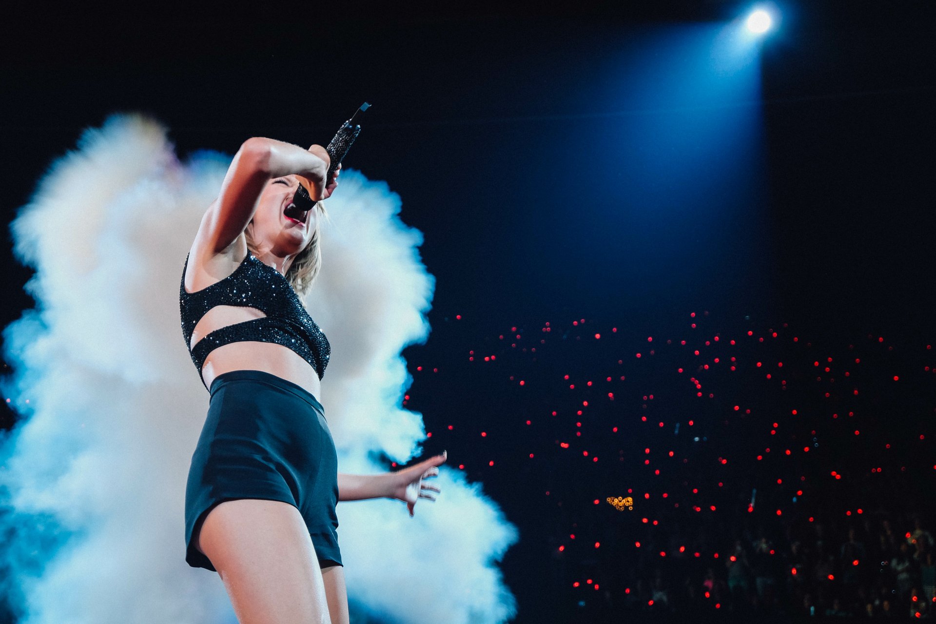 Blonde American singer performing onstage with microphone, surrounded by stage smoke and blue lighting — 4K Ultra HD PC desktop wallpaper.