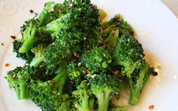 Seasoned broccoli florets on a white plate, vibrant food photo rendered in 4K Ultra HD PC desktop wallpaper background.
