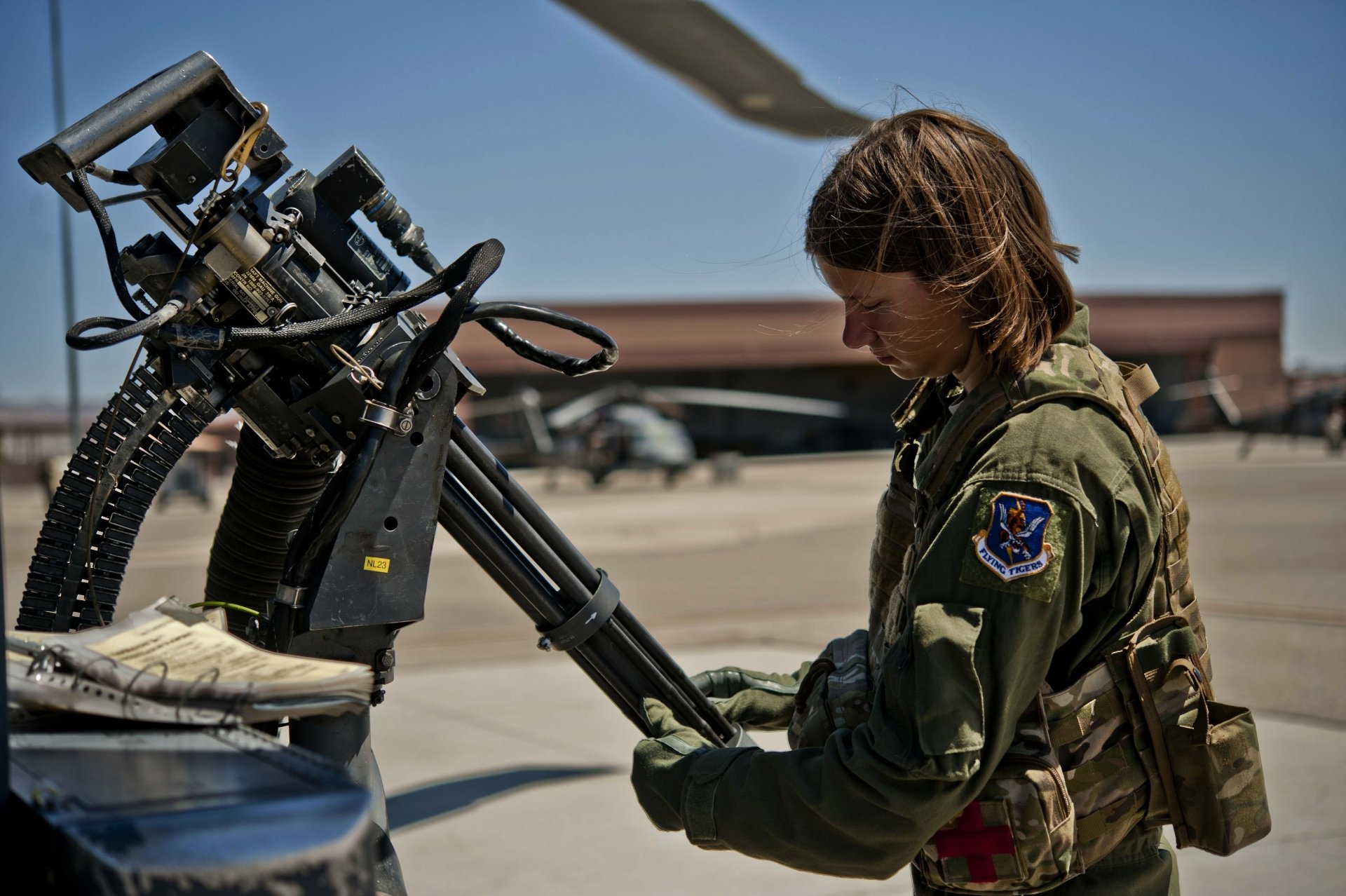 A soldier in military attire prepares a machine gun on an aircraft, set against a clear blue sky, showcasing a moment of tactical readiness in a 4K Ultra HD backdrop.