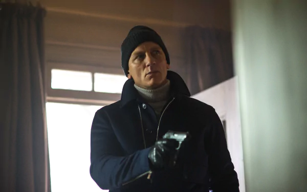 Daniel Craig as James Bond in a tense moment from the movie Spectre, gripping a gun while dressed in a dark coat and beanie, set against a dimly lit background.